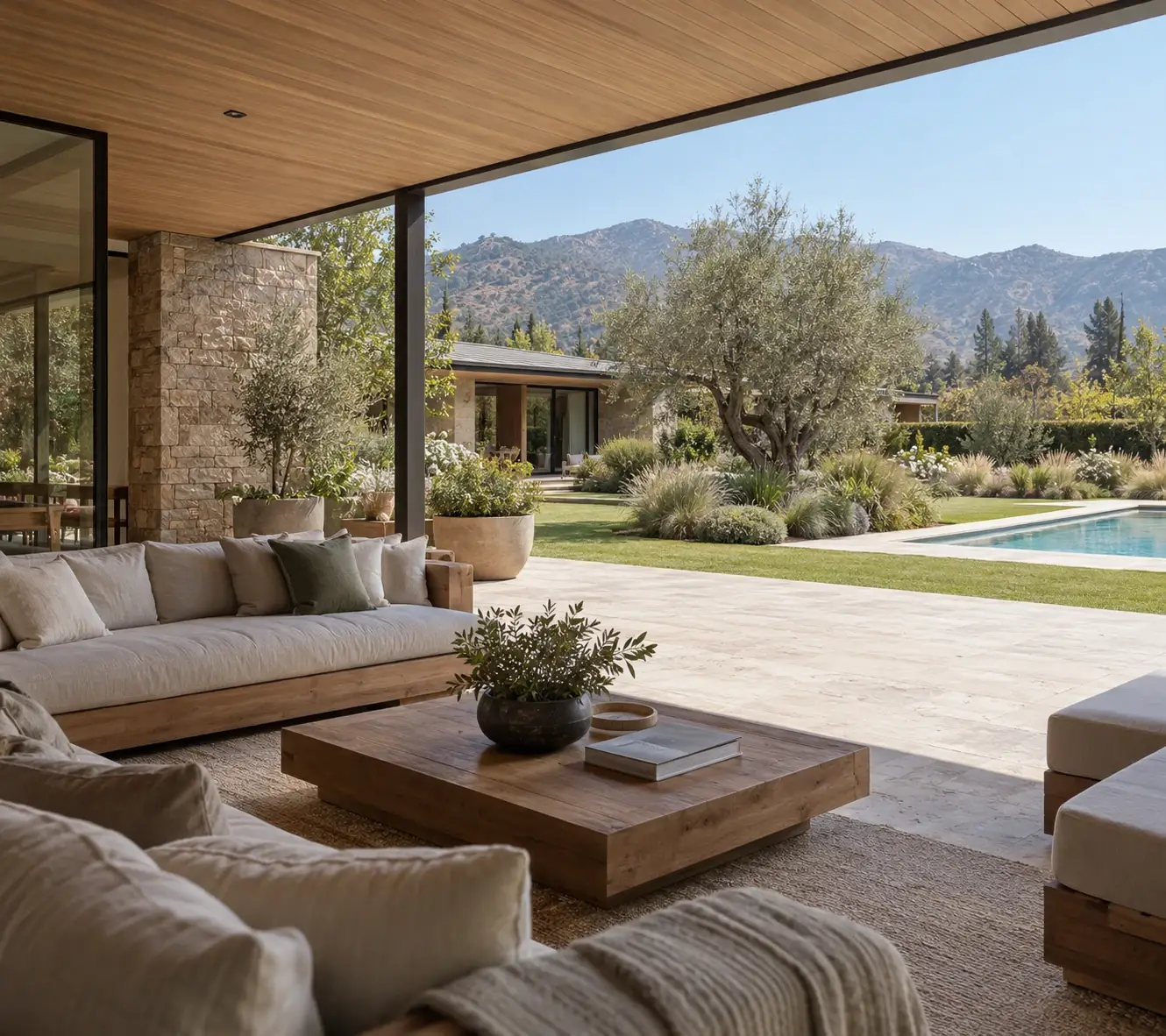 Terraza de madera y piedra abierta a un jardín con piscina y vista a los cerros